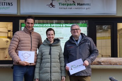 Drei Menchen stehen vor der Gastronomie, zwei halten weiße Schilder in der Hand