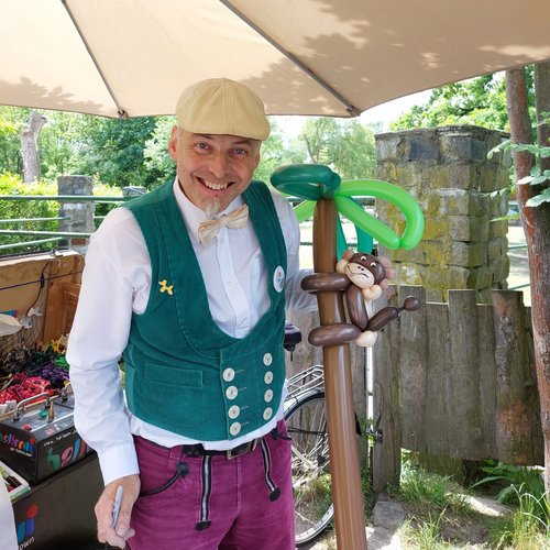 Mann mit lustig bunten Klamotten bastelt ein Ballon mit einem Affe